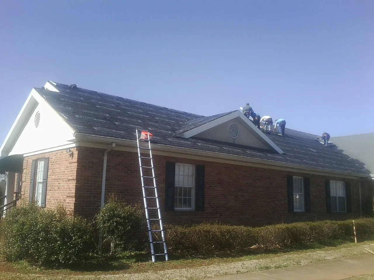 Crew tearing shingles off a brick ranch roof with a ladder set — Metal Roof Repair work by our crew in Rohrersville