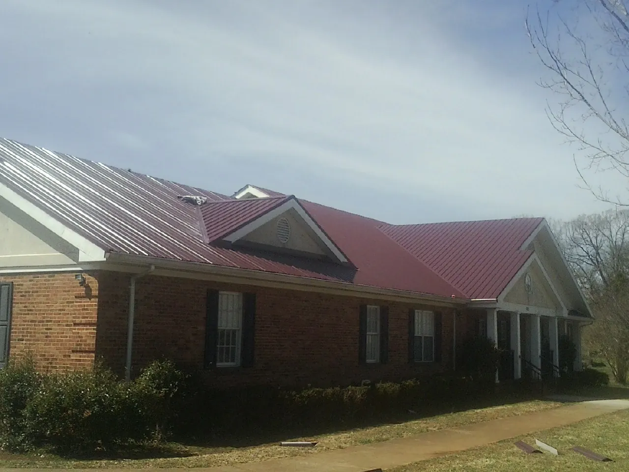 Red metal roof with gabled entries on a long brick building, from a Hail Damage Roof Repair job in Rohrersville
