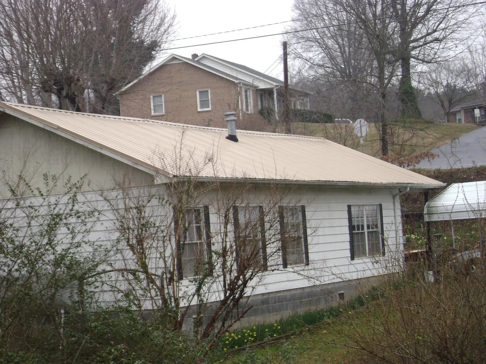 Tan metal roof on a white sided house set into a hillside — Commercial Roofing by Roofing Brothers in Rohrersville